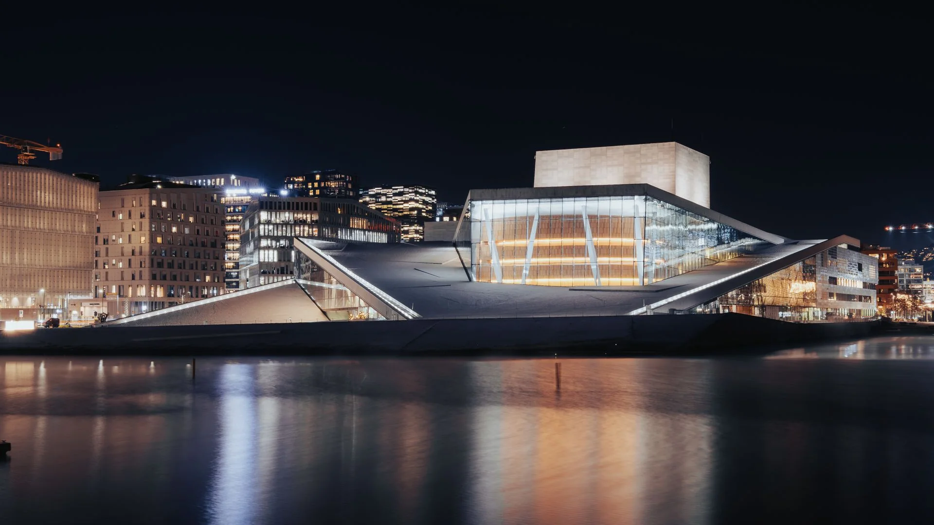 The Oslo Opera House lit up at night, its glass foyer glowing above the dark water of the fjord