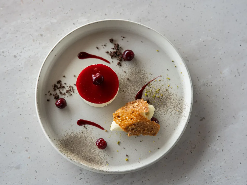 A berry dessert with a red coulis and a small crumb of biscuit on a round grey plate